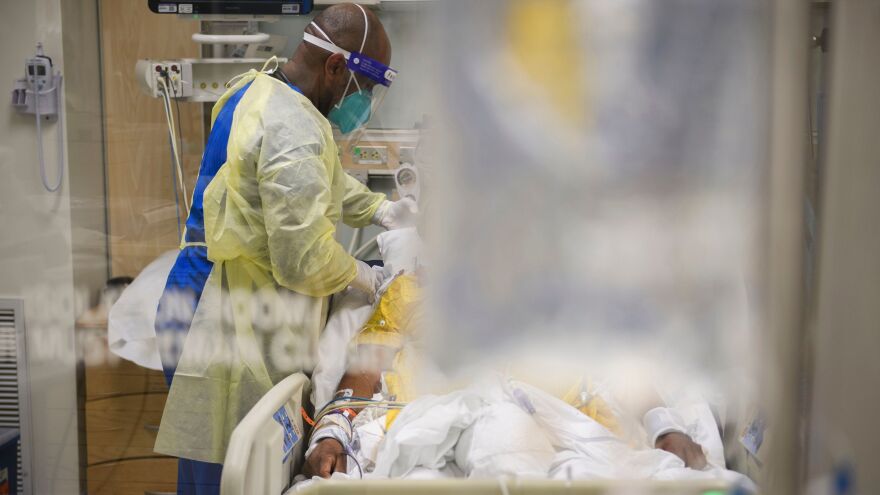 A Black man in full protective medical gear attends to a patient in a hospital ER.