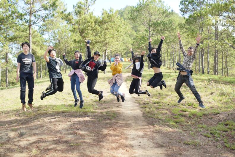 A row of pre-teens jump in the air and smile. They are outdoors on what appears to be a nature hike.