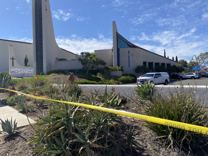 Yellow caution tape stretches along a stucco wall next to the parking lot. The church building is visible beyond it.