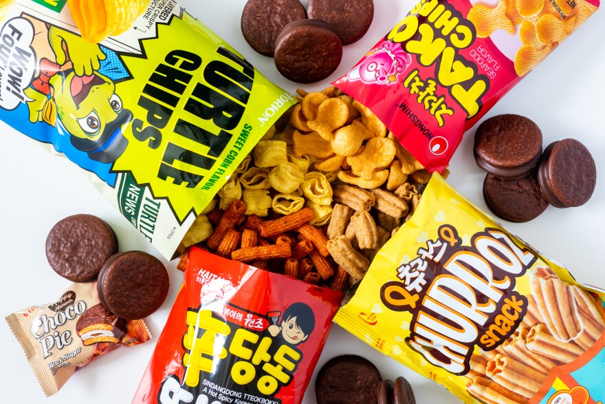 Several bags of Korean snack food poured out onto a white surface. Between each snack bag is a small pile of choco pies and chocolate-dipped sandwich cookies.
