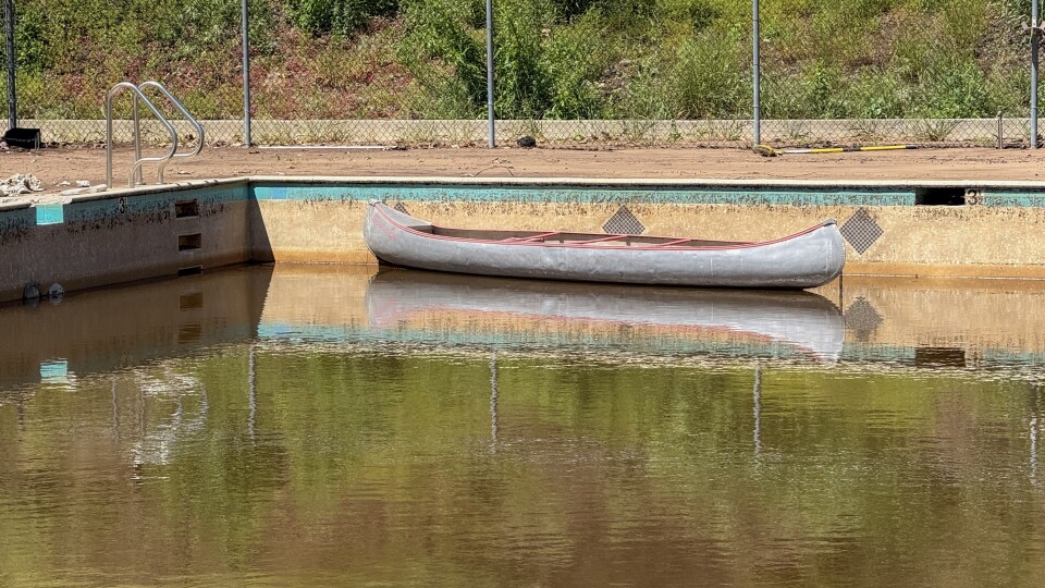 A metal canoe sits in a fire-damaged pool filled with brown murky water 