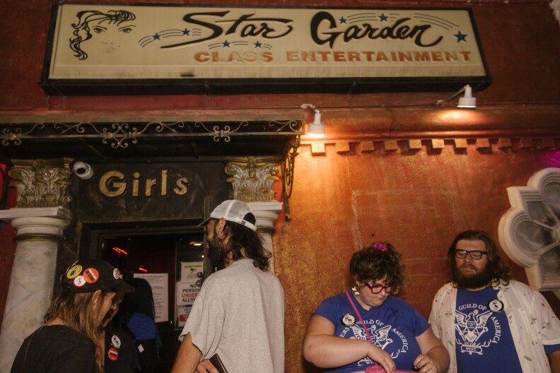 The night-time exterior of the Star Garden strip club in North Hollywood and a sign promising "class entertainment": Patrons are lined up waiting to walk through an entrance that says "Girls" in large gold letters