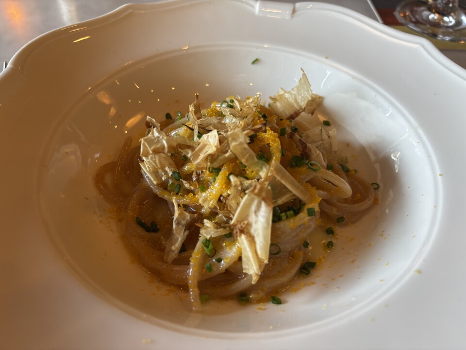 A spaghetti dish topped with bonito flakes, light papery shavings of dried fish common in Japanese cuisine, and shaved bottarga, cured fish roe in the form of orange powdery flakes, topped with chopped chives. 