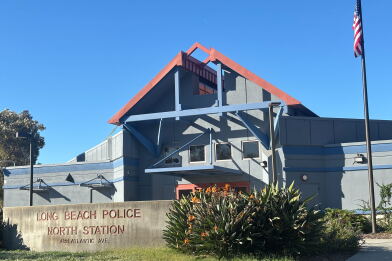 A concrete sign reads "Long Beach Police North Station" in front of a building with a peaked roof overhang and U.S. flag on a tall pole.
