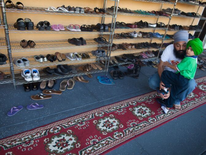Amarpreet Singh-Malik removes the shoes from his three-year-old son Gurdaas outside the prayer room at the Khalsa Care Foundation on Monday, August 6.