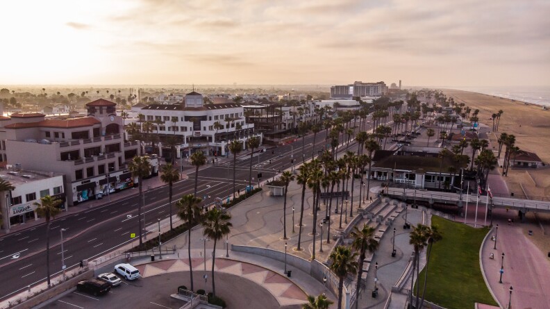 A view of a low-lying city area with a beach on the right and streets largely vacant. Palm trees line street and park areas.