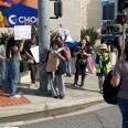 Protesters on a street corner hold signs with slogans that include "Politicians should not make healthcare decisions," "Patients before politics" and "Trust doctors."