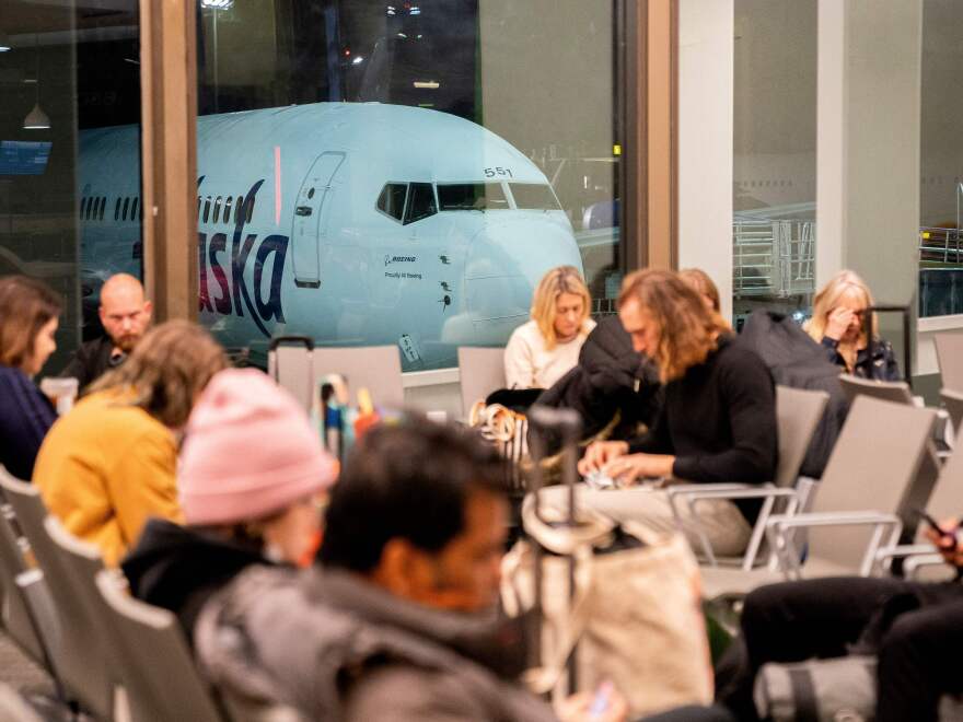 Travelers wait in the terminal as an Alaska Airlines plane sits at a gate at Los Angeles International Airport early Thursday.