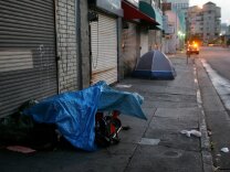 LOS ANGELES, CA - APRIL 19:  A police car stops near homeless people sleeping in their encampments in the early morning hours of downtown sidewalks on April 19, 2006 in Los Angeles, California. Most homeless tents and improvised shelters are taken down at dawn, before their possessions can be hauled away by cleaning crews. A 9th U.S. Circuit Court of Appeals panel ruled last week that a city law making it illegal to sleep or sit on city sidewalks cannot be implemented as long as there is a shortage of homeless shelter beds in Los Angeles. According to a study released in January by the Los Angeles Housing Services Authority, there are nearly 90,000 homeless people live in Los Angeles County but only 9,000 to 10,000 beds available in homeless shelters, single-room occupancy hotels, and other facilities.    (Photo by David McNew/Getty Images)