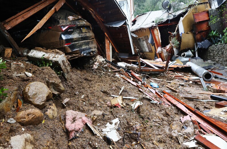 A car is smashed under a collapsed roof as mud and debris pilesalng other damaged structures.