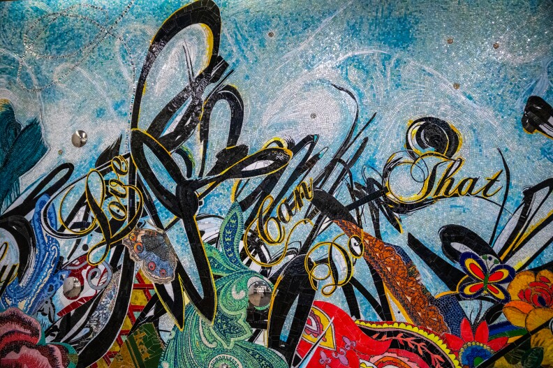 A colorful tile mosaic shows butterflies and flowers and swooping black lines reminiscent of graffiti art, along with stylized words in cursive that read "Love can do that."