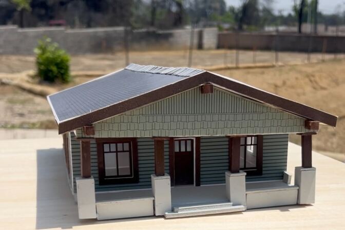 A scale model of a green home with a front porch and dark brown roof. 