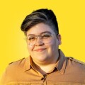 A portrait of Caitlin Hernández, smiling, against a yellow background.