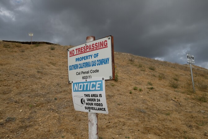 A sign on a brown grass hill reads "no trespassing property of socal gas" under stormy skies. 