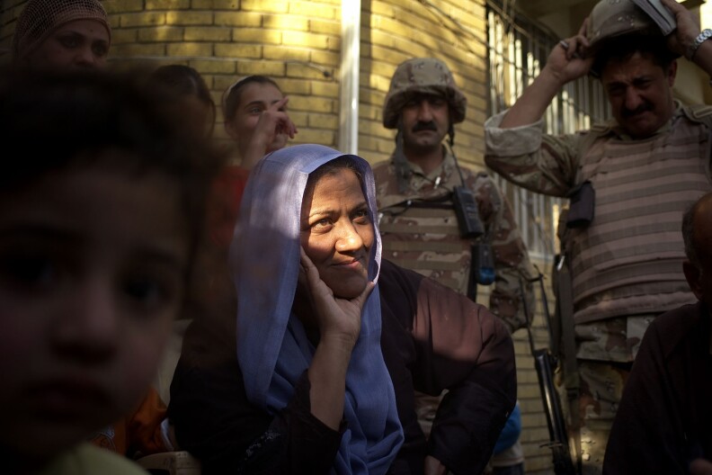 Sunni Suada (Su'ada) Soadoun, b. 1958, smiles to American and Kurdish soldiers after they stopped her from being evicted by a Shiite militia for a third time from her house in Kaadamiya, Baghdad, on March 27, 2007...The previous day American and Kurdish soldiers rushed to Suada Soadoun's house after she called the Kurdish soldiers to complain men were trying to evict her for the third time. ..The soldiers arrived and detained two of the men, a third escaped on foot. Suada is a widow, with four daughters and many grandchildren, and without a man to make her case for her, she fought and argued with the men who had tried to throw her out of her house. ..The men were masquerading as workers from the Ministry of finance, but their documents were false and they were carrying a pistol. It is impossible to say, but it is most likely they were members of the Mahdi army militia. ..The US and Kurdish soldiers left with their detainees and the street cheered and clapped their unlikely heros. Less than 18 hours later Suada was shot eight times by assassins on a motorcycle outside a bakery just over a block from her home. (Photo by Ashley Gilbertson / VII Network)