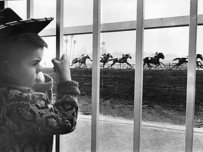  Photograph article dated January 31, 1963 partially reads, "The original object, of course, was not to create the youngest racetrack tout in American, but to impress on a soft, 6-year-old mind that gamblers die of malnutrition. This was the highly commendable purpose. Somewhere, in the paddock at Santa Anita perhaps, it went astray." Wells A. Twombly Jr. watching the horse race. 