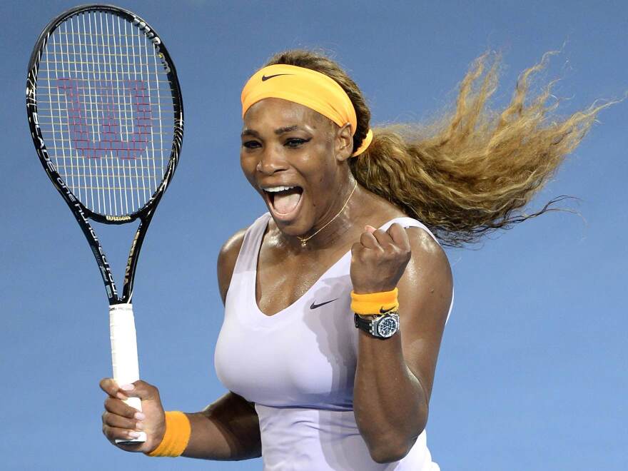 Tennis player Serena Williams smiles with her tennis racket in one hand and a balled fist in the other.