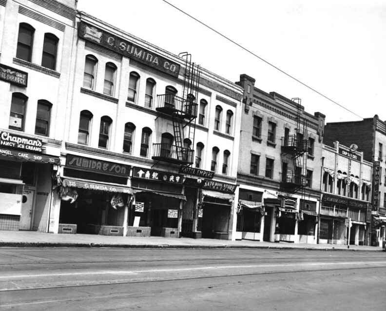 A black and white photo of the older buildings with fire escapes out front, includes street level shops and restaurants along First Street in Little Tokyo.