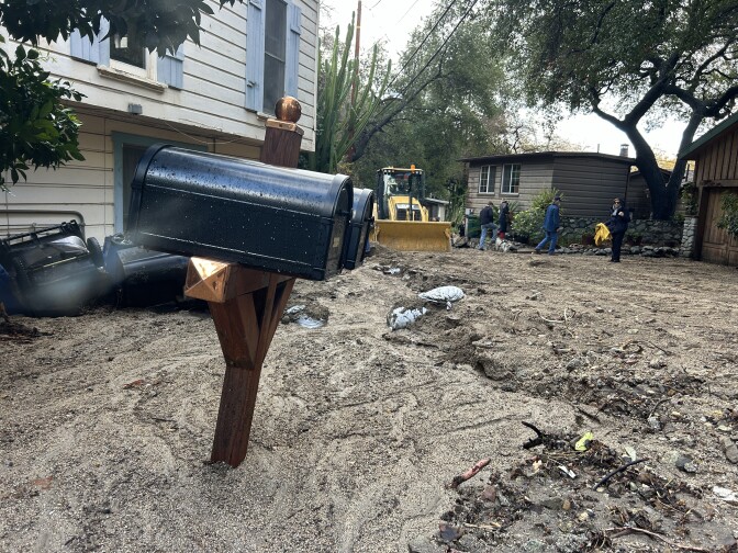 The front area of a home is full of mud and a mailbox is partially buried in it. 