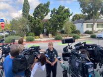 Sheila Kuekl in a short-sleeved button-down shirt is surrounded by media