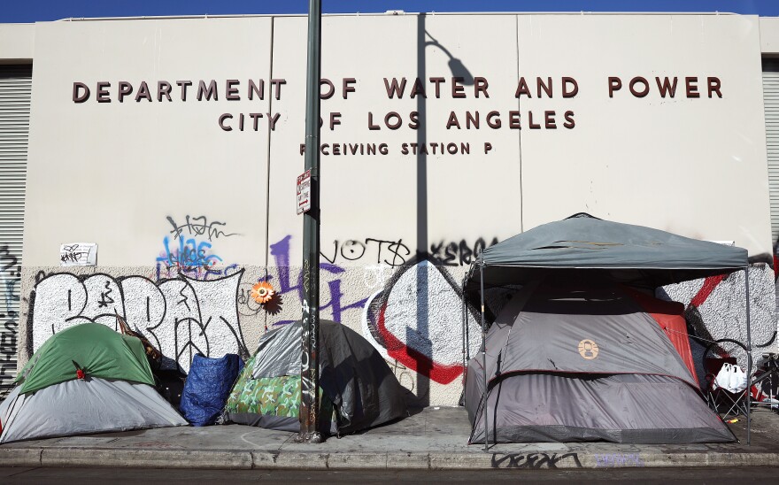 Three tents set up on a sidewalk in front of a beige building with grafitti and signage that reads, "Department of Water and Power City of Los angeles receiving station P."