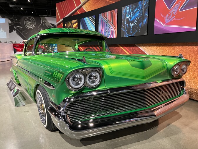 A bright-green 1950s-era classic car; in the backdrop are colorful art pieces on an earth-toned wall.