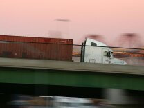 LONG BEACH, CA - JULY 06:  A truck carries a shipping container at the ports of Long Beach and Los Angeles on July 6, 2006 in Long Beach, California. In the Los Angeles area, studies indicate that diesel exhaust from trucks, locomotives, heavy equipment and ships causes cancer and is responsible for 70% of pollution-related health problems and hundreds of deaths every year. Rather than wait for the international agency that regulates the global shipping industry, the International Maritime Organization, to implement considered changes to strengthen emissions standards for cargo vessels, the ports recently unveiled an ambitious clean-air plan that could significantly improve air quality. The proposal seeks to reduce diesel emissions from cargo ships, trains and trucks by more than 50% over a five-year period at a cost of $2-billion.Almost 5,800 ships called at the ports of Los Angeles and Long Beach in 2005 released about 14,000 tons of air pollutants. Many ships emit as much exhaust per day as 12,000 cars.  (Photo by David McNew/Getty Images)