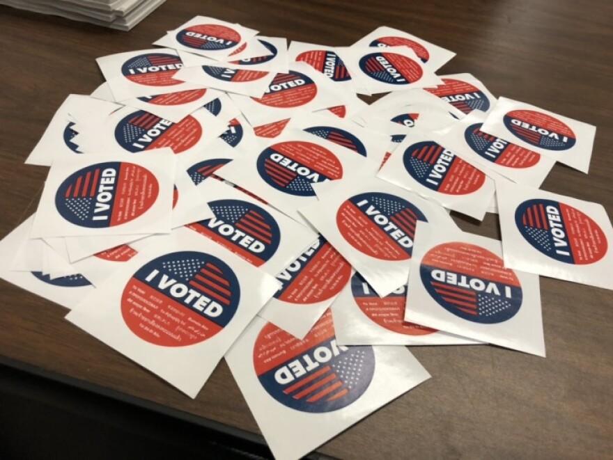 A pile of 'I Voted' stickers is spread across a wooden table.