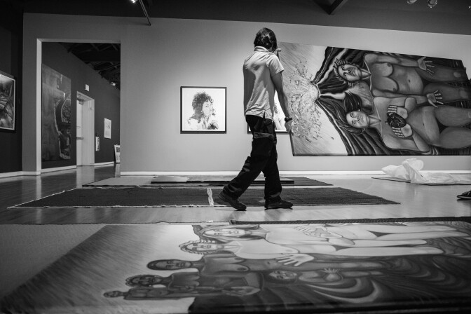 a black and white photo of a person with their back to the camera walking through a gallery with some art on the walls and some on the floor