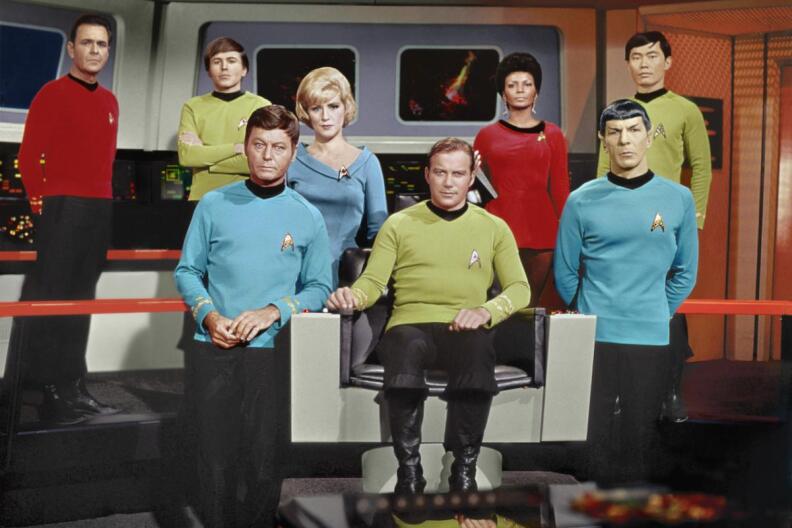 The original cast of the original Star Trek including Kirk, Spock, Sulu and Uhura sits or stands on the bridge of the Enterprise, wearing their Star Fleet uniforms