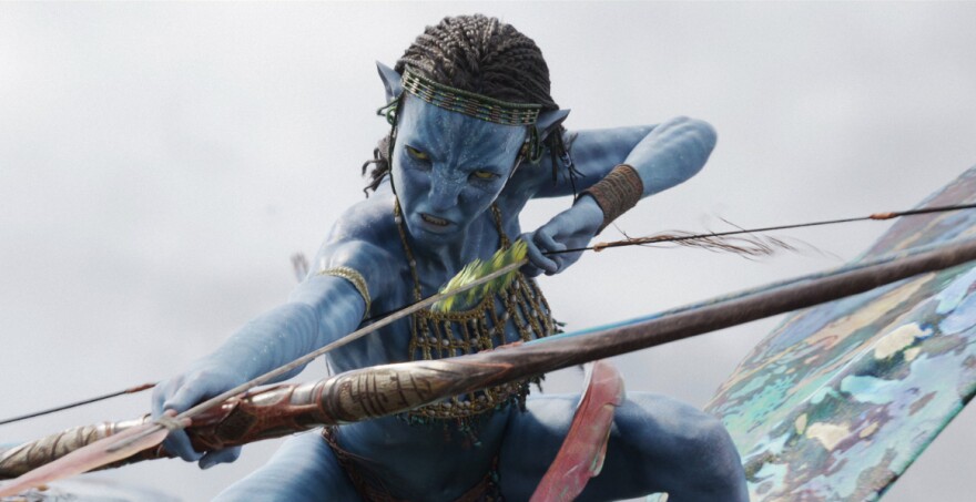 The blue-skinned character of Neytiri in "Avatar: The Way of Water", is readying a bow and arrow with a determined look on her face