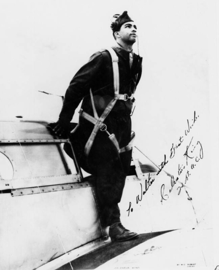 A man with medium-tone skin postes in uniform on a plane