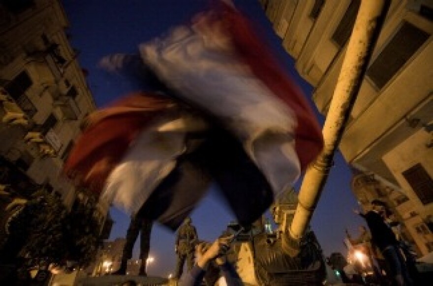 Anti-government protesters wave Egyptian flags in front of an army tank as demonstrators at Cairo's Tahrir Square react after President Hosni Mubarak stepped down on February 11, 2011.