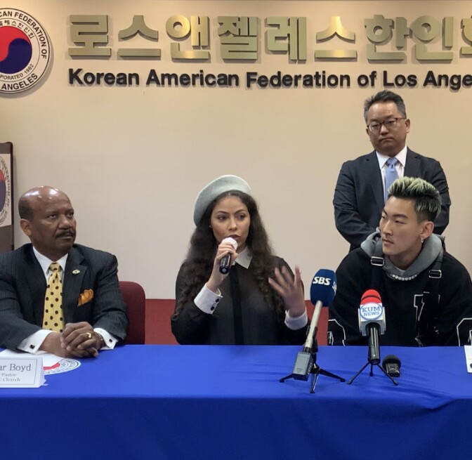 A Black woman in her 30s is flanked by a middle-aged Black man to her left and an Asian man in his 20s or 30s on her left. 