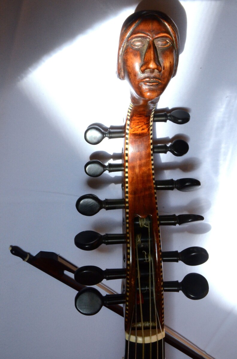 The carved head and peg box of an early 18th-century Baryton, a bass viol with additional metal strings that change the instrument's timbre. 
