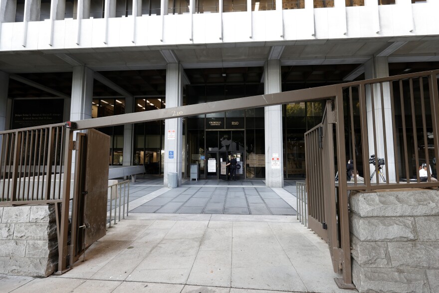 A building with a white facade and tall block columns sits behind a gated entrance that's open.