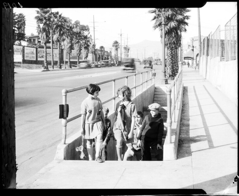 A black and white image from 1927 shows children walking up stairs to a sidewalk as automobiles are visible in the background.