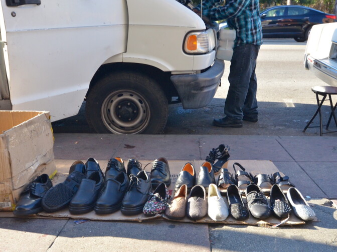The sidewalks are lined with merchandise and the vendors' cars and vans line the curb along Alvarado Street.