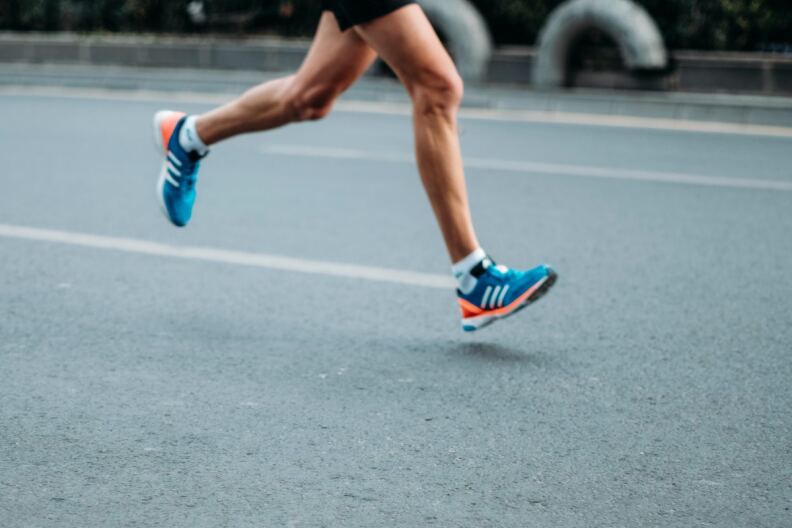 A pair of legs in blue running shoes runs on pavement.