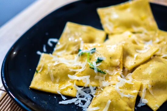 Ravioli with some light cheese shredded over top sits in a black bowl.