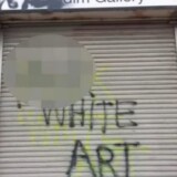 A vandalized garage door in Boyle Heights, with the words "expletive" white art spray painted on. 