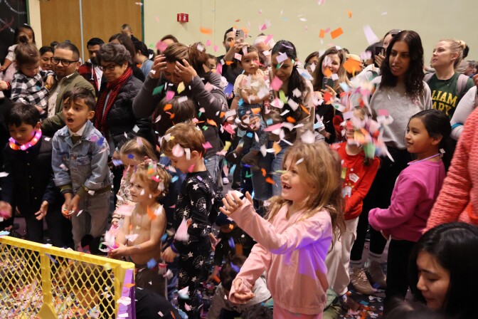 Children exclaim as adults watch on as confetti falls from above. 