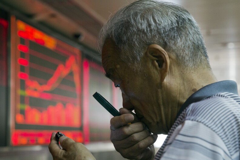 A Chinese investor uses a magnifying glass to look at his mobile phone screen as he monitors stock prices at a brokerage house in Beijing, China, Thursday, July 9, 2015. Asian stock markets continued to react on Thursday as the Chinese government took measures aimed at stabilizing the market. (AP Photo/Ng Han Guan)