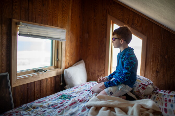 A boy in his bed and he looks out the window.