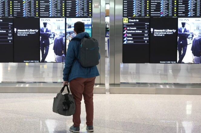 a person with a backpack and a bag looks at a board of flight information