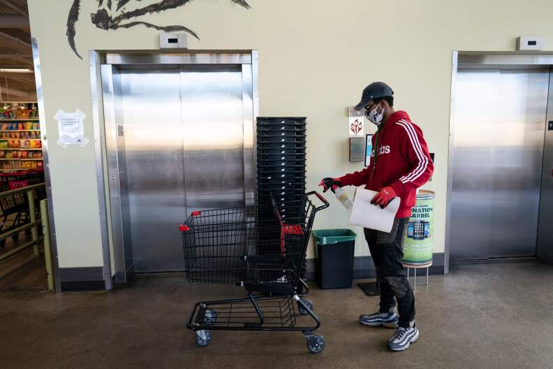 A person with a mask on sprays a shopping cart while standing by an elevator.