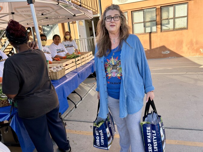 Female presenting person holds two bags. She wears a blue, long sleeved shirt.