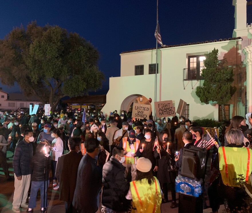 Hundreds of people gather in front of San Gabriel Mission for a vigil. People are holding candles and you can see signs that read "United We Stand" and "Fight Against Hatred."