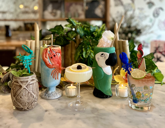 Five tiki-themed cocktails are displayed on a table in Le Fe bar. One of the glasses features a red lobster. Another is made in the shape of a green parrot.