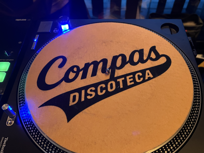 A yellow turntable mat says "Compás Discoteca". It is illuminated by a blue light on the left side.